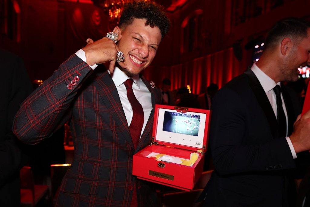 Patrick mahomes cargando la cajita de los anillos por un lado y enseñando los anillos con la otra mano.